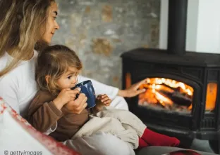 Vrouw met kind op schoot voor de kachel